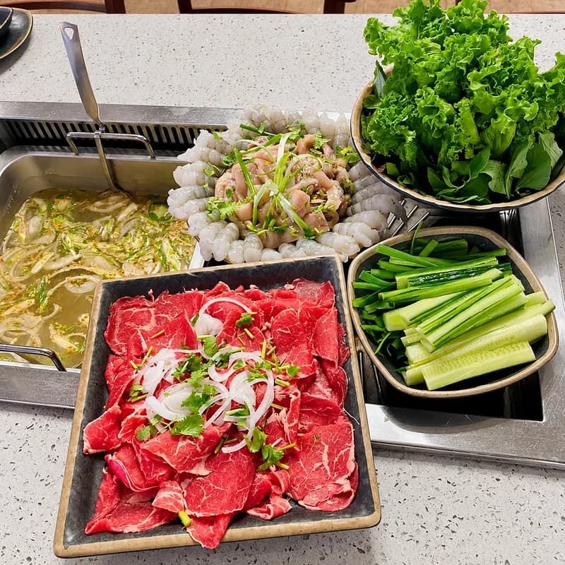 Raw sliced ribeye on a platter beside the grill with lettuce, cucumber and scallions