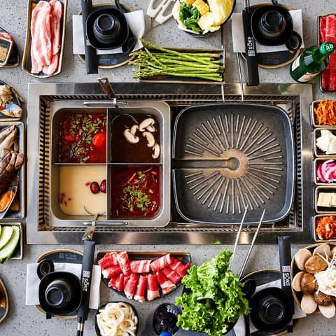 A Sōke table set for a group: split hot pot, grill, meats, vegetables and side dishes