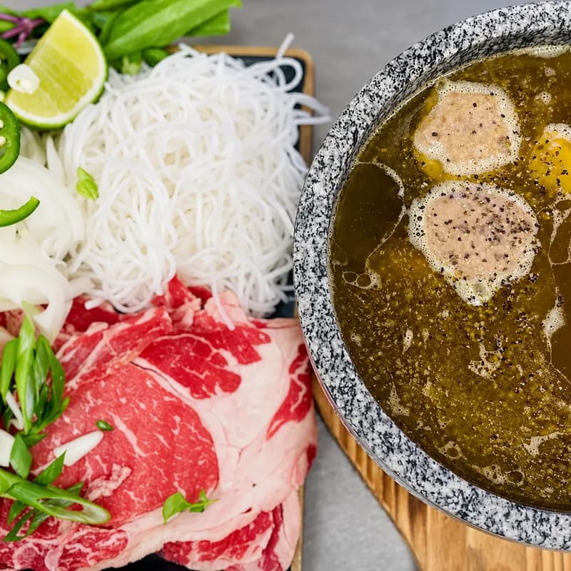 Stone pho with sliced ribeye and bubbling beef broth in a hot stone bowl