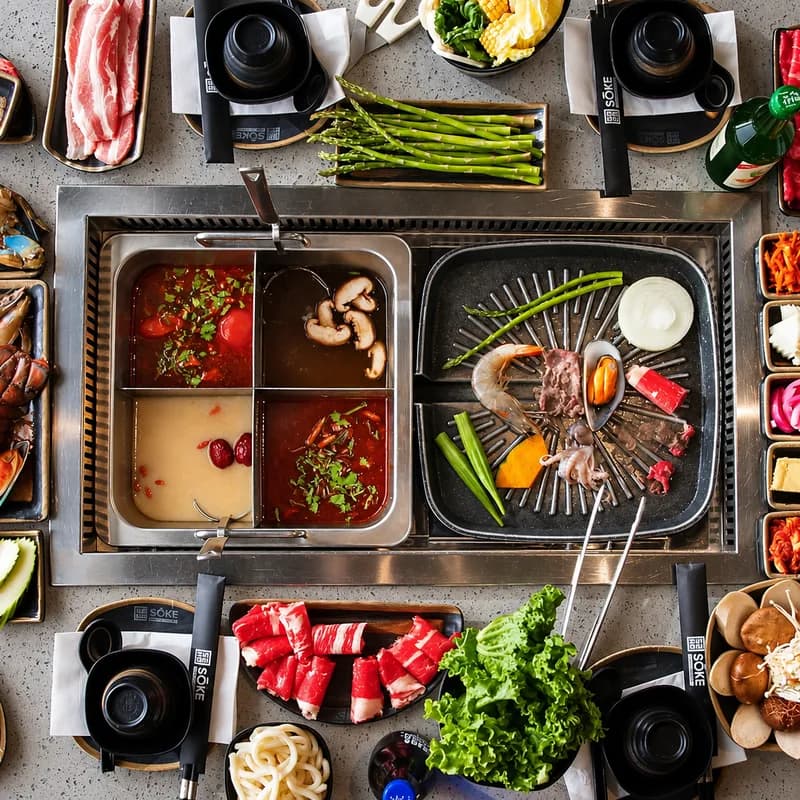 A full Sōke table from above: split hot pot, tabletop grill, raw meats, seafood, vegetables and side dishes