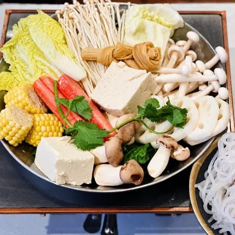 A hot pot filled with napa cabbage, tofu, mushrooms, corn and noodles